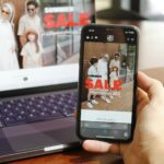 A person holding a cell phone in front of a laptop